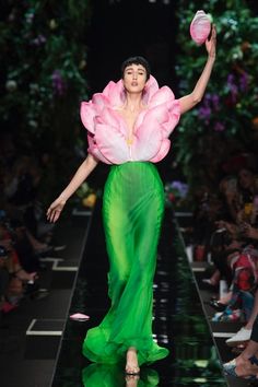 a woman is walking down the runway in a green dress with pink flowers on it