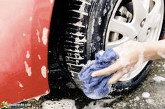 a hand with a rag on it washing a red car's wheel and tire