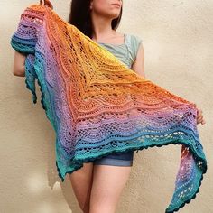 a woman is holding up a multicolored crocheted shawl in front of a wall