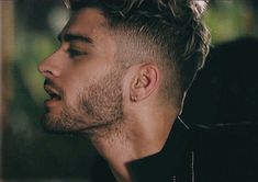 a man with curly hair and piercings looks off to the side while wearing a black jacket