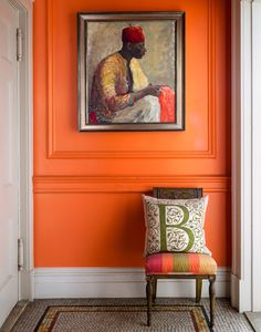 an orange room with a painting on the wall and a chair in front of it