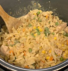 a pot filled with pasta and vegetables next to a wooden spoon