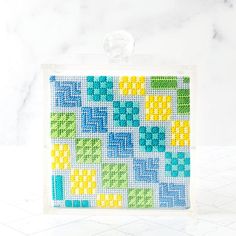 a cross - stitch pattern on a glass block with a white marble countertop in the background