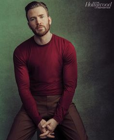 a man in a red shirt and brown pants is sitting on a stool with his legs crossed