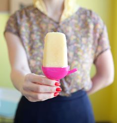 a woman is holding a pink and white ice cream cone in her right hand while wearing a blue skirt