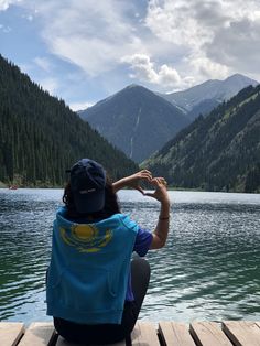 a woman sitting on top of a wooden dock next to a lake with mountains in the background