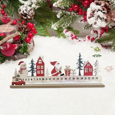 a wooden calendar sitting on top of a snow covered ground next to christmas decorations and pine cones