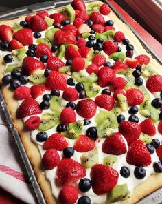 a pizza topped with kiwis, strawberries and blueberries on top of a pan