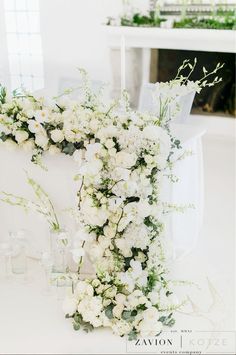 white flowers and greenery are arranged on the back of a chair at a wedding