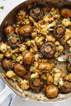 a pan filled with mushrooms and cauliflower on top of a table next to a spoon