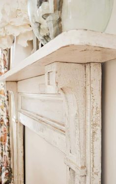 an old white fireplace mantel with glass vase on top