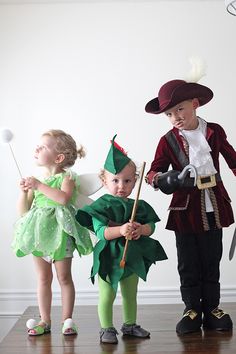 three children dressed in costumes standing on a wooden floor