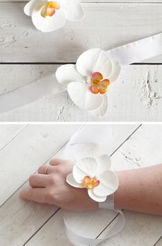 two white flowers with yellow centers are being held by someone's hand on a white wooden surface