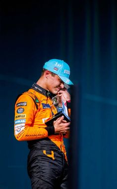 a man in an orange shirt and blue hat holding a cell phone to his ear