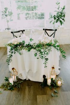 the table is set with candles and greenery for an elegant wedding reception in white