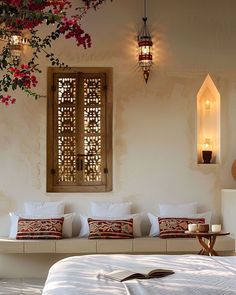 a bed with white sheets and pillows next to a wall mounted window filled with red flowers