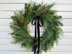 a wreath hanging on the side of a white wall with pine cones and evergreens