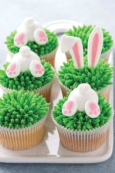 cupcakes decorated with green frosting and white bunny ears are on a tray