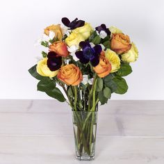 a vase filled with lots of different colored flowers on top of a wooden table next to a white wall