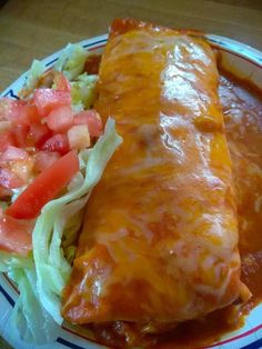 a burrito and salad on a plate with dressing, lettuce and tomato