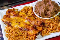 a white plate topped with rice and meat next to a bowl of sauce on top of it