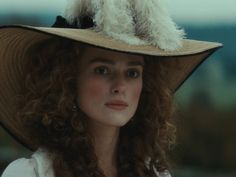 a woman wearing a large hat with a dog on it's head and long curly hair