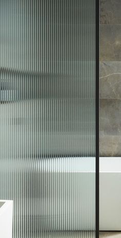 a white bath tub sitting next to a tall glass shower door with vertical blinds on it's side