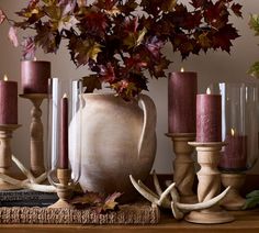 an arrangement of candles, vases and antlers on a mantle with autumn leaves