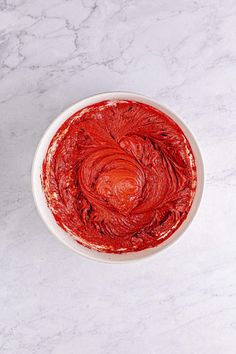 a white bowl filled with red food on top of a marble countertop next to a knife and fork