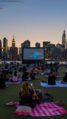 many people are sitting on the grass watching movies in front of a cityscape