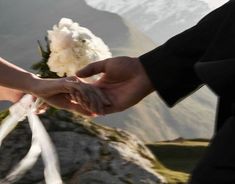 the bride and groom hold hands as they stand on top of a mountain