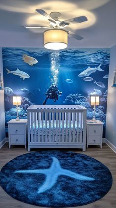 Underwater-themed nursery with a fish mural, white crib, changing table, blue rug, and light wood floors, in a Ocean Nursery Theme, Underwater Nursery, Stylish Ceiling Fan, Nautical Theme Nursery, Gender Neutral Nursery Design, Nursery Design Neutral, Jungle Themed Nursery, Ocean Themed Nursery, Dreamy Nursery