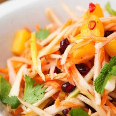 a white bowl filled with carrots, cranberries and cilantro garnish