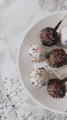 chocolate covered cake pops with sprinkles and white frosting on a plate