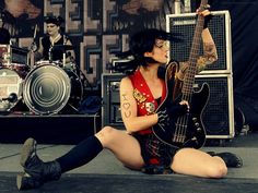 a woman sitting on the ground with a guitar in front of her and other instruments behind her