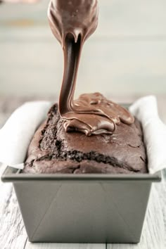 a chocolate cake in a pan being drizzled with melted chocolate on top