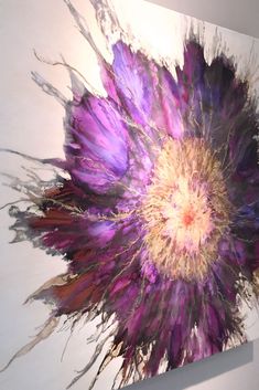 a large purple flower is hanging on the wall in front of a white wall with an abstract painting behind it