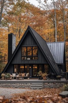 a black house in the woods surrounded by fall foliage and trees with leaves on the ground