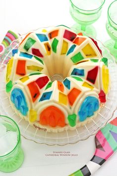 a colorful cake sitting on top of a glass plate next to other plates and glasses