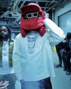 a man wearing a red hat and sunglasses is standing in front of other people with his hands on his head