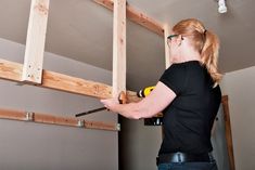 a woman in black shirt working on wooden frame with drill and screwdriver next to ladder