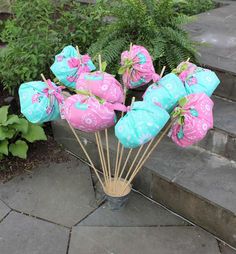 a bunch of pink and blue balloons sitting on top of a wooden stick in front of some plants