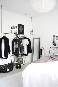 a bedroom with white walls and clothes hanging on the rack in front of the bed