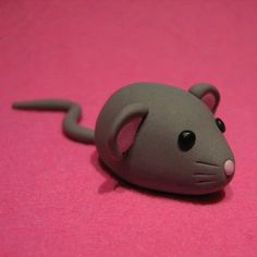 a small gray toy mouse sitting on top of a pink surface with one eye open