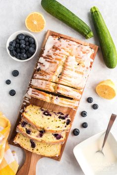 sliced loaf of lemon blueberry bread on a cutting board next to fresh berries and cucumbers