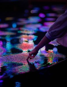 a person touching something on the ground with colorful lights in the background and water droplets all around them