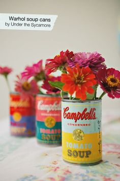 three cans with flowers in them sitting on a table