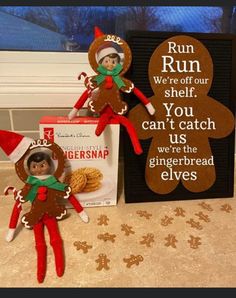 two elfs are sitting next to a gingerbread sign and a box of cookies