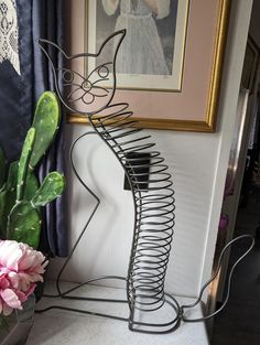 a metal cat sculpture sitting next to a potted plant and painting on the wall