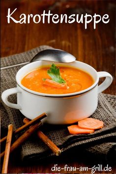 a white bowl filled with carrot soup next to cinnamon sticks